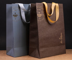 Картонні пакети «Le Silpo» - особливі тим, що два принципово різні стилі: еко-пакет з крафт паперу  та ламінований пакет з картону ми поєднали в одну лінійку з допомогою вишуканого тиснення золотою фольгою та конгреву. Матова ламінація доповнює неповторність та вишуканість сірого кольору. Світло- сірі широкі атласні ручки, приємні на дотик і міцно закріплені у спеціально вирізаних отворах гармонійно підійшли обом стилям.